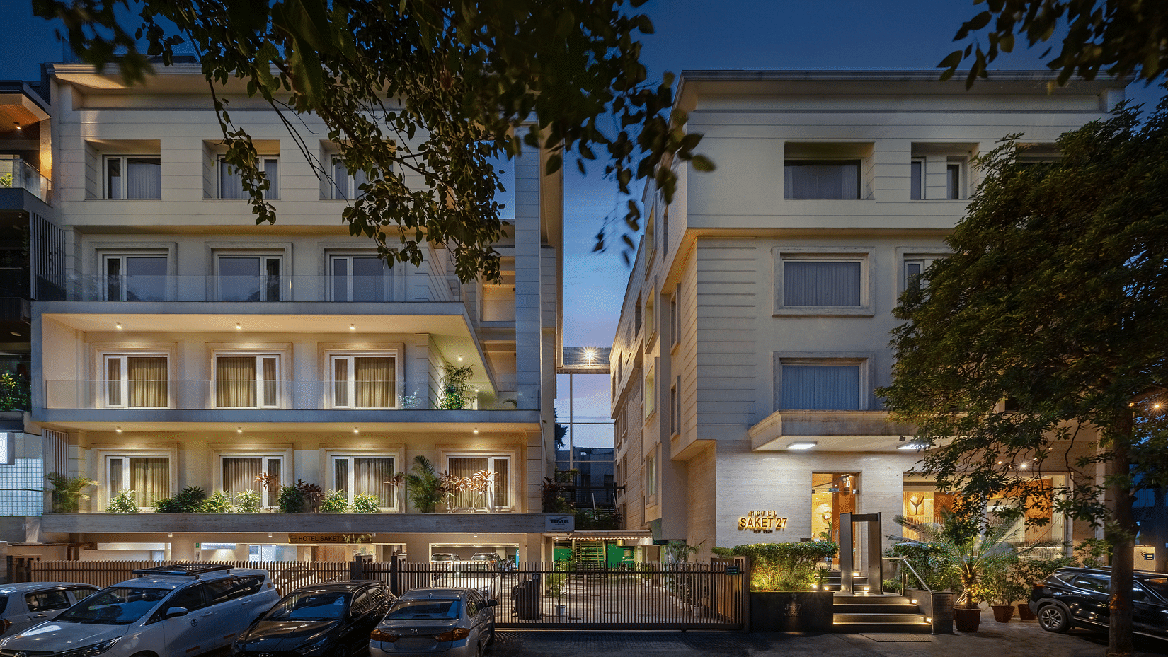 Exterior view of Hotel Saket 27 in Delhi, India. The hotel is a modern building with warm lighting and a well-maintained entrance.